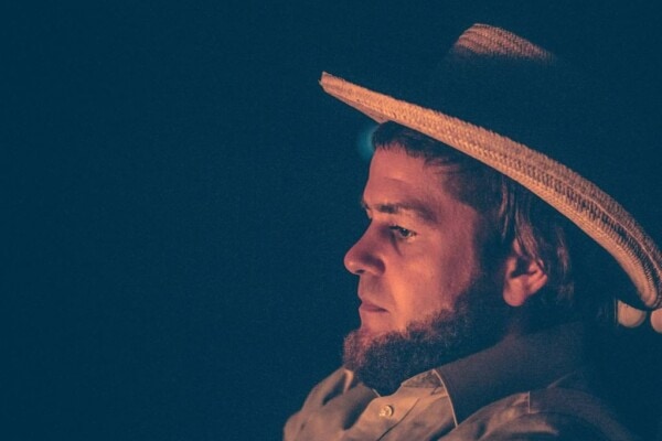 Amish man wearing a hat in front of a fire