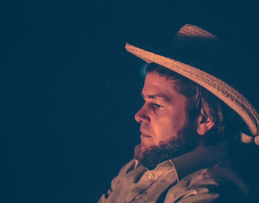 Amish man wearing a hat in front of a fire