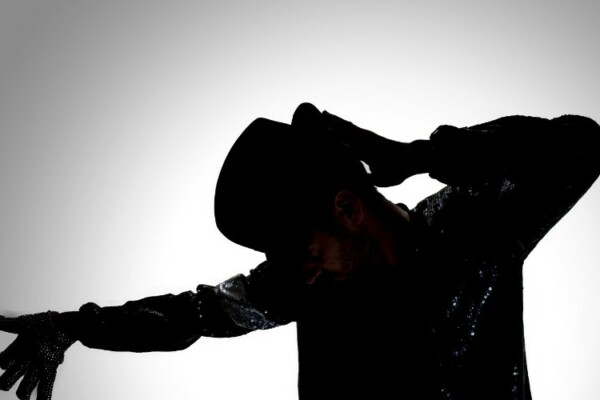 man posing in the shadows as Michael Jackson with his iconic hat and costume