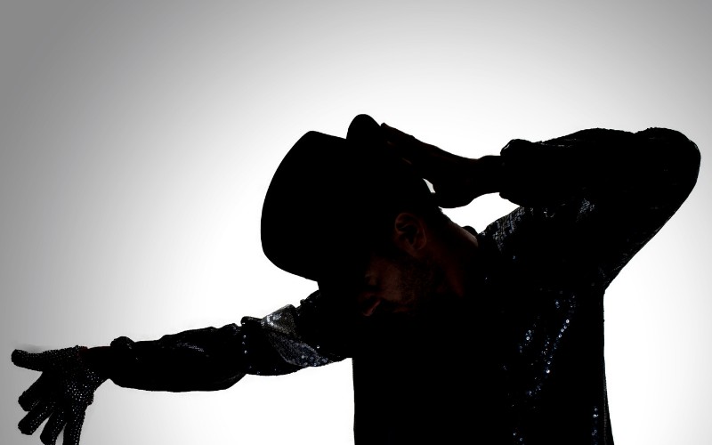 man posing in the shadows as Michael Jackson with his iconic hat and costume