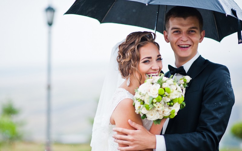 couple getting married under the rain  holding a black umbrella