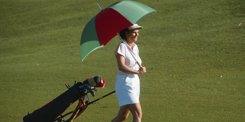 Woman playing golf carrying a golf umbrella