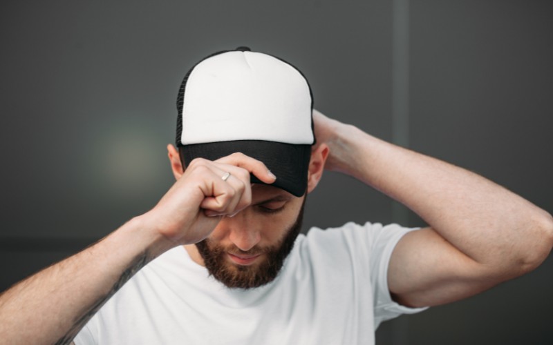 Man placing a black and white baseball cap on his head.